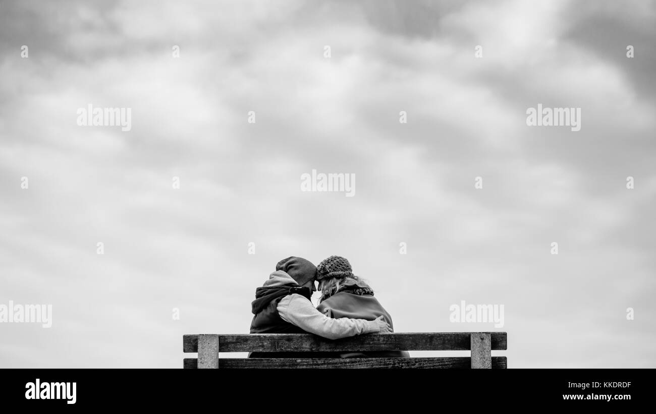 Romantic couple in love sitting on a bench on the Howth`s pier hugging and kissing, Howth Peninsula, Dublin, Ireland Stock Photo